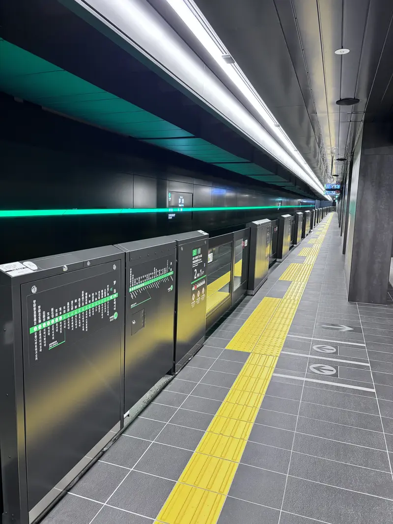 近未来的で誰もいない駅のホーム。プラットホームドアが設置されており、壁には緑色のライン照明が一直線に伸びている。